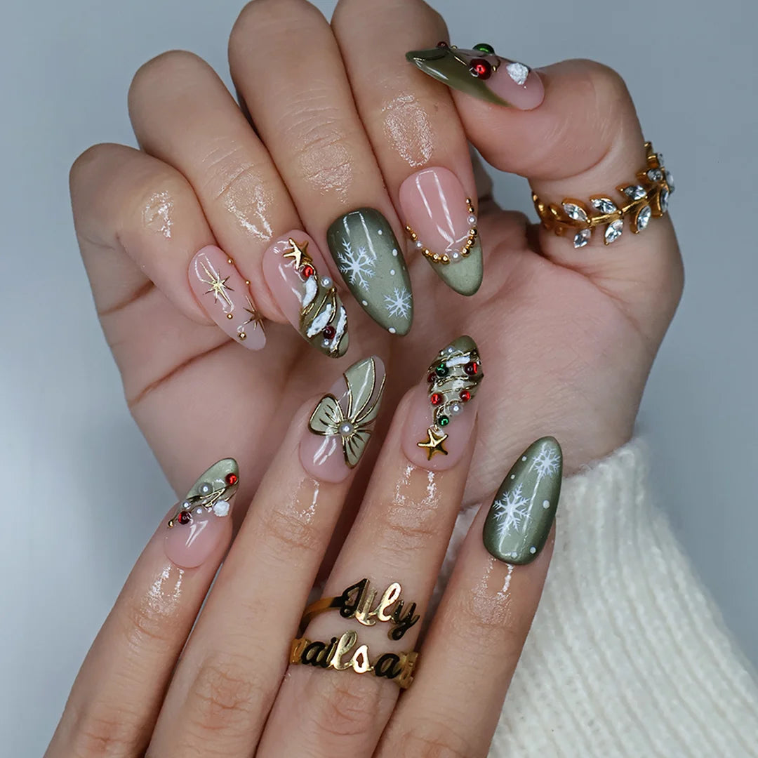 Wintergreen handmade Christmas press-on nails — medium almond set in nude and sage-green cat-eye with a 3D gold-star Christmas tree, delicate snowflakes, gold bow, ornament baubles and red-green gemstone accents.