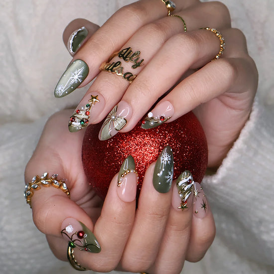 Wintergreen handmade Christmas press-on nails — medium almond set in nude and sage-green cat-eye with a 3D gold-star Christmas tree, delicate snowflakes, gold bow, ornament baubles and red-green gemstone accents.
