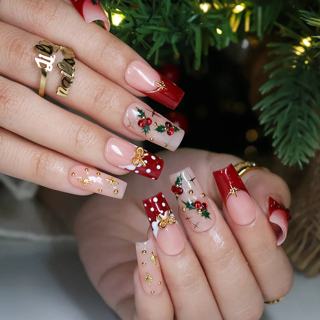 Hollytini handmade Christmas press-on nails — medium square set in nude and red with holly berries, gold bows, gold starbursts, white polka dots and sparkling red gemstone accents.