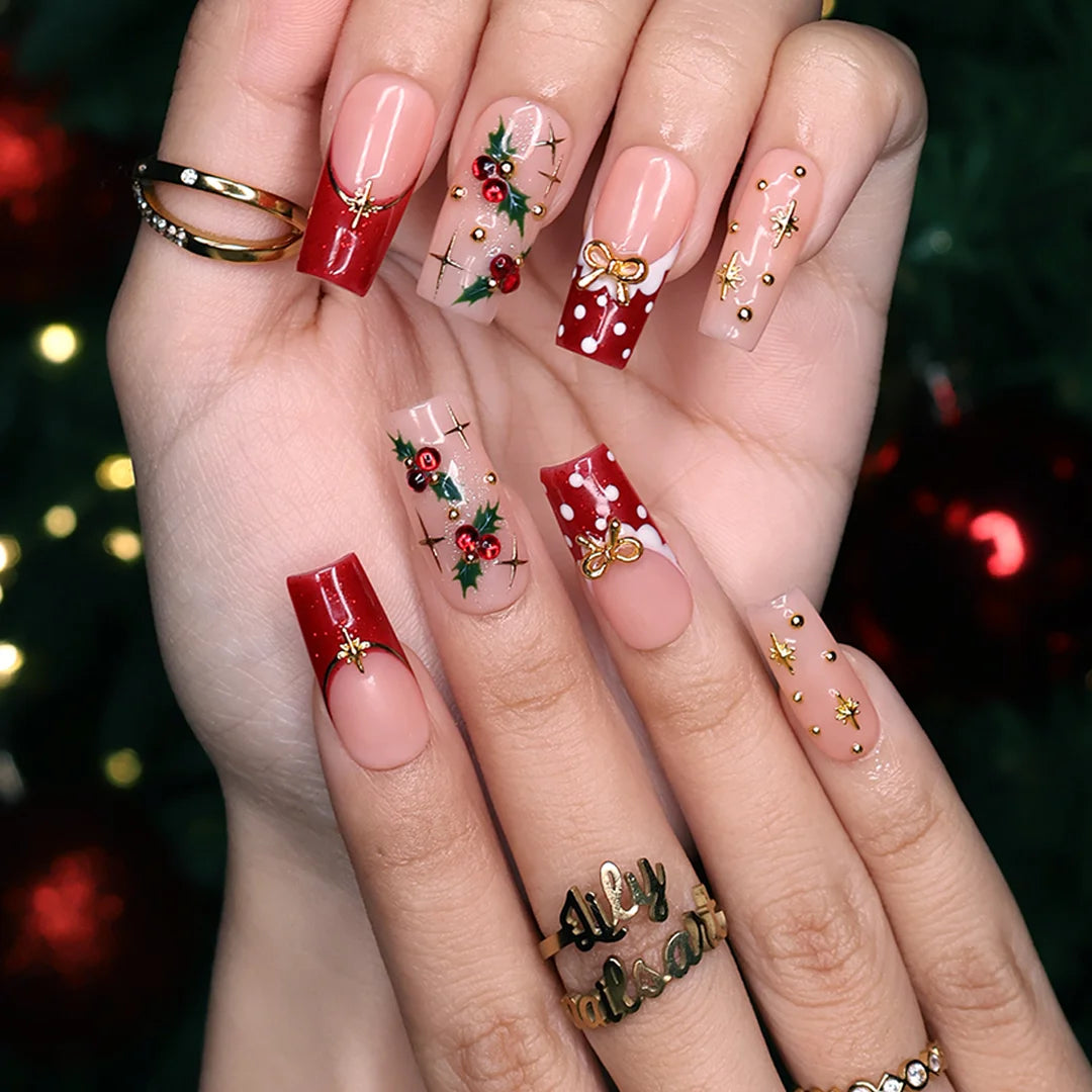 Hollytini handmade Christmas press-on nails — medium square set in nude and red with holly berries, gold bows, gold starbursts, white polka dots and sparkling red gemstone accents.