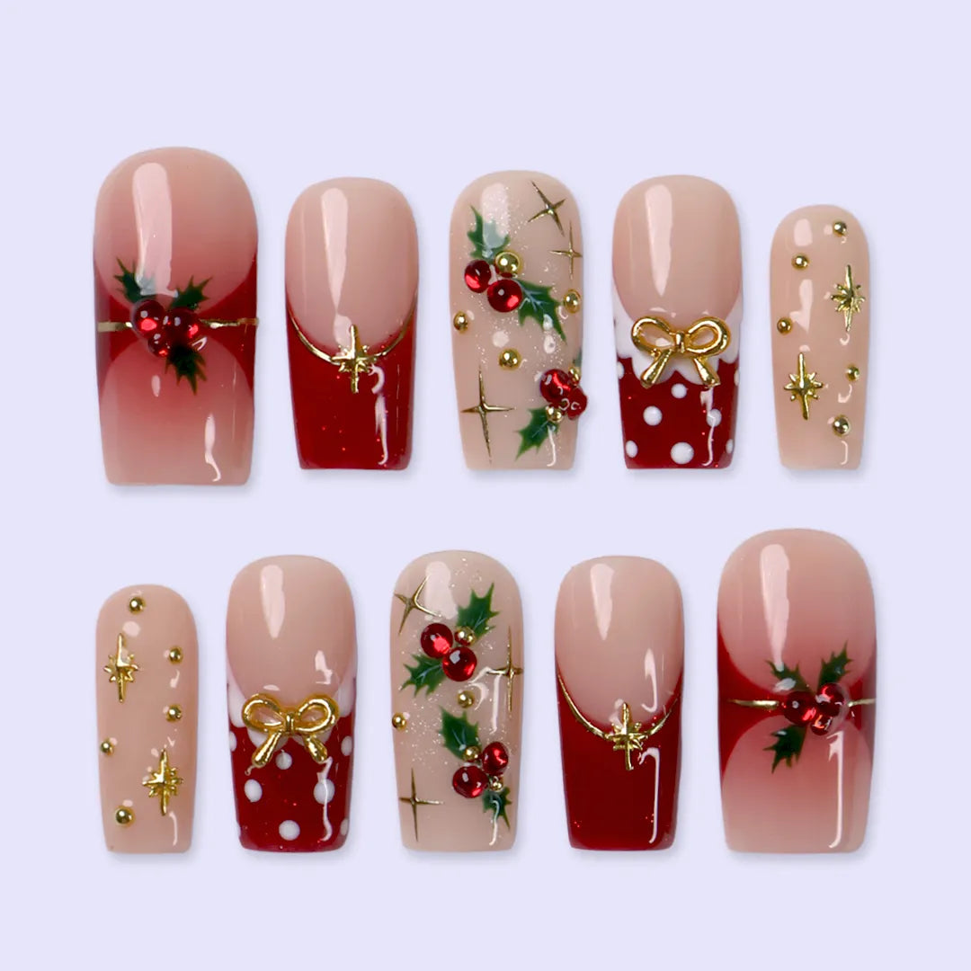 Hollytini handmade Christmas press-on nails — medium square set in nude and red with holly berries, gold bows, gold starbursts, white polka dots and sparkling red gemstone accents.