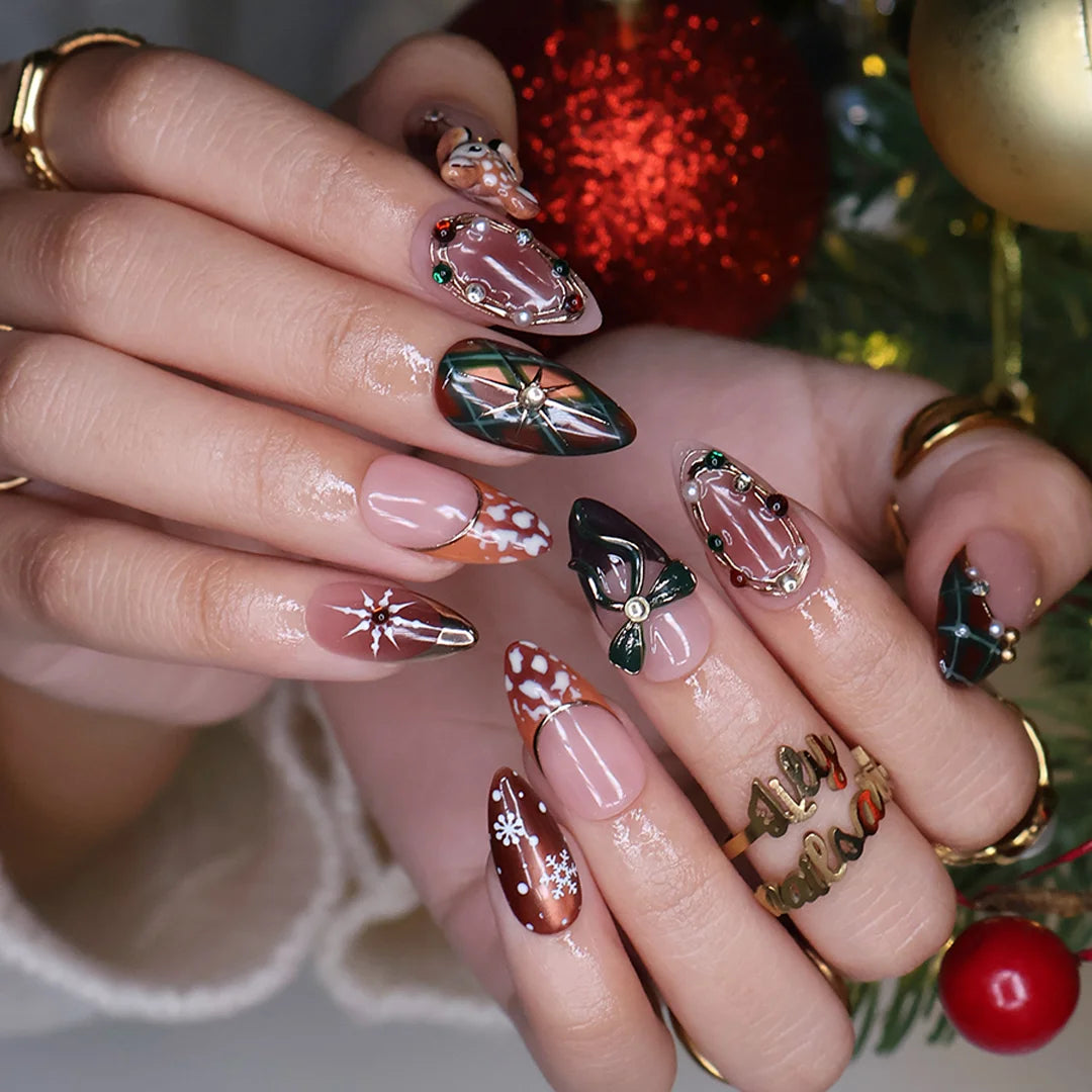 Fawnelle handmade Christmas press-on nails — medium almond set in nude, caramel-brown and green with a 3D baby deer, green bow, cozy plaid, fawn-spot patterns, delicate snowflakes and gold-framed gemstone accents.