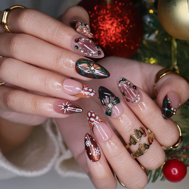 Fawnelle handmade Christmas press-on nails — medium almond set in nude, caramel-brown and green with a 3D baby deer, green bow, cozy plaid, fawn-spot patterns, delicate snowflakes and gold-framed gemstone accents.