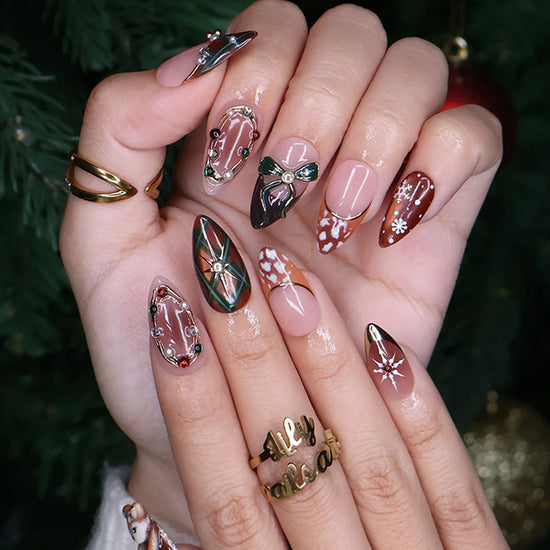 Fawnelle handmade Christmas press-on nails — medium almond set in nude, caramel-brown and green with a 3D baby deer, green bow, cozy plaid, fawn-spot patterns, delicate snowflakes and gold-framed gemstone accents.