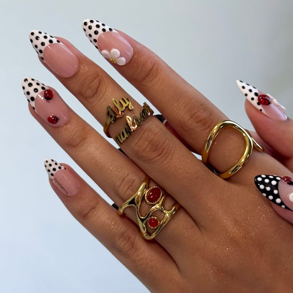 Hand with polka dot nail design and gold rings on a light gray background