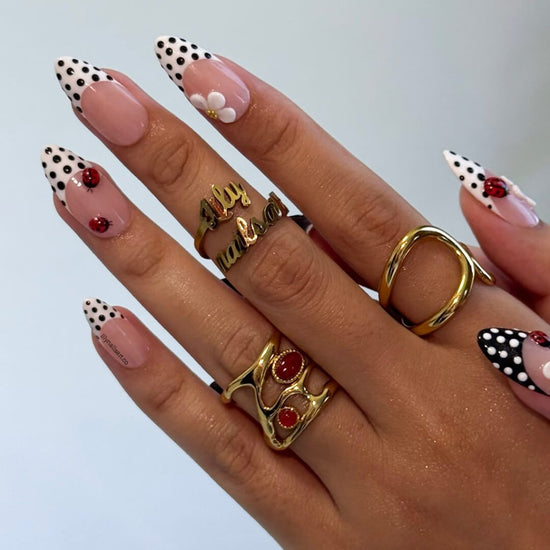 Hand with polka dot nail design and gold rings on a light gray background