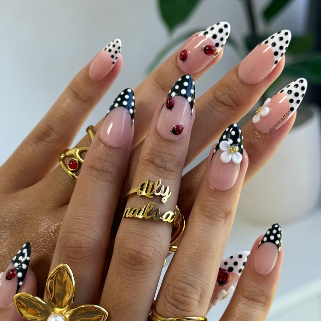 Nails with polka dot and floral designs, wearing gold rings, on a neutral background.