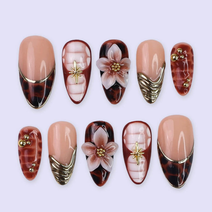 Luxury press-on nails with tortoiseshell patterns, 3D florals, and gold metallic accents on warm amber and nude bases — handmade medium almond nails — perfect for elegant everyday wear, chic autumn looks, or timeless luxury nail art.
