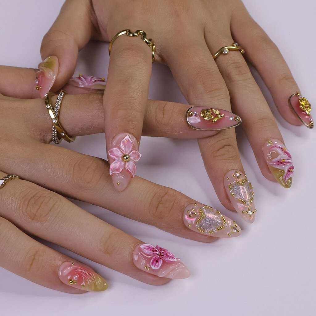 A spring press-on nail set wear by a hand model with shimmering hearts, blooming lily florals, and golden rose accents. Bathed in soft pinks and warm blush tones, this set sparkles with delicate gems and dreamy textures, capturing the essence of pure, elegant love. ✨ perfect for weddings, Valentine's Day, or anniversaries.