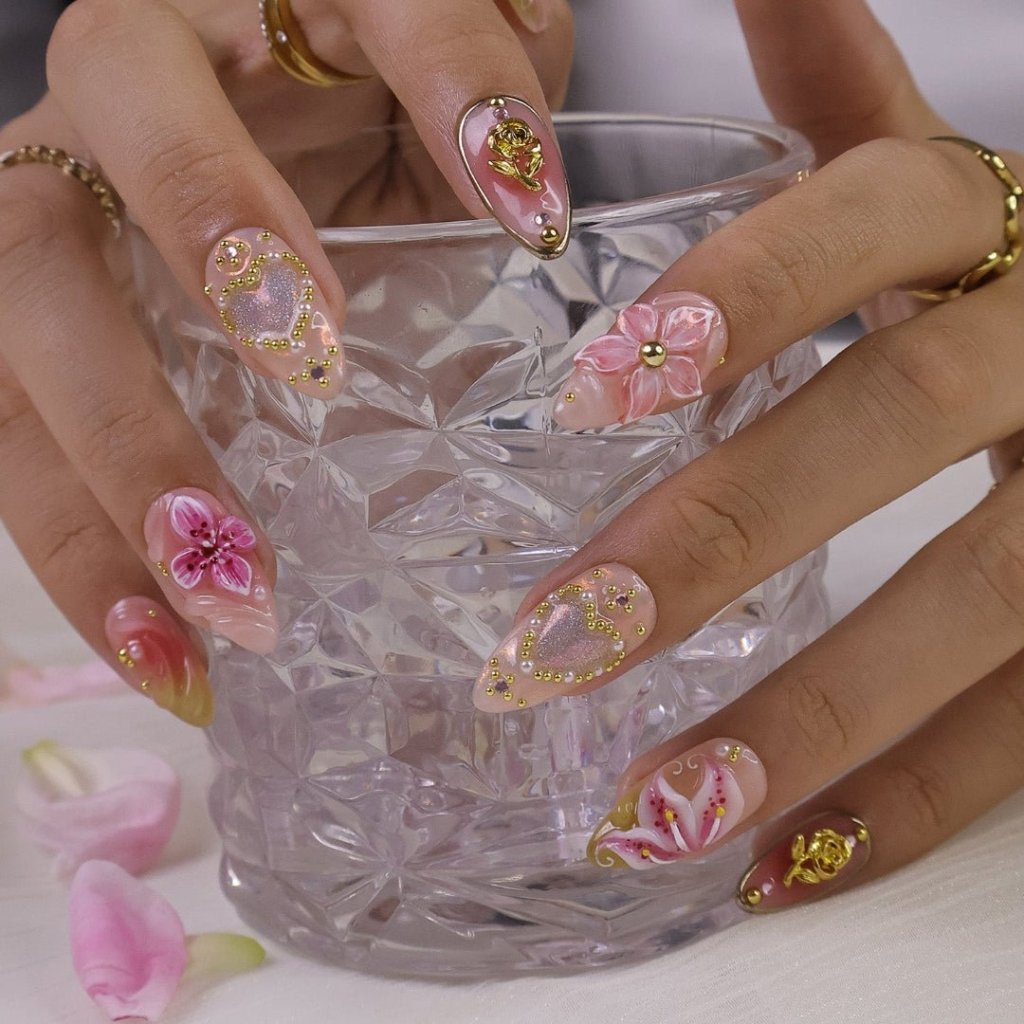 A spring press-on nail set wear by a hand model with shimmering hearts, blooming lily florals, and golden rose accents. Bathed in soft pinks and warm blush tones, this set sparkles with delicate gems and dreamy textures, capturing the essence of pure, elegant love. ✨ perfect for weddings, Valentine's Day, or anniversaries.