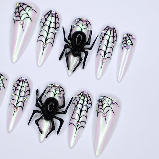 White chrome stiletto Halloween press on nails with 3D black spiders, spiderweb line art, and iridescent crystal accents — handmade spooky press-ons, custom fake nails for Halloween parties, creepy cute nail art, horror fashion aesthetic.