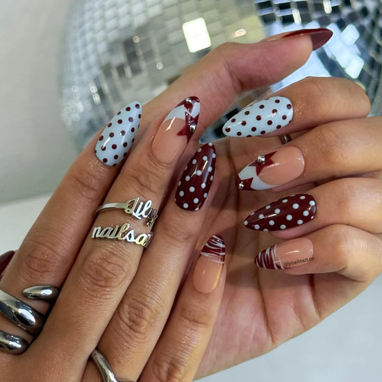 Handmade almond press on nails featuring a playful mix of burgundy polka dots, nude base with burgundy geometric tips, silver bead accents, and abstract line art. Retro-inspired, perfect for a bold and stylish look.